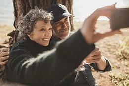 Man and woman sitting together outdoors at campsite and taking selfie