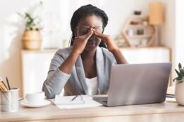 lady sitting at a desk with eye strain looking at a laptop