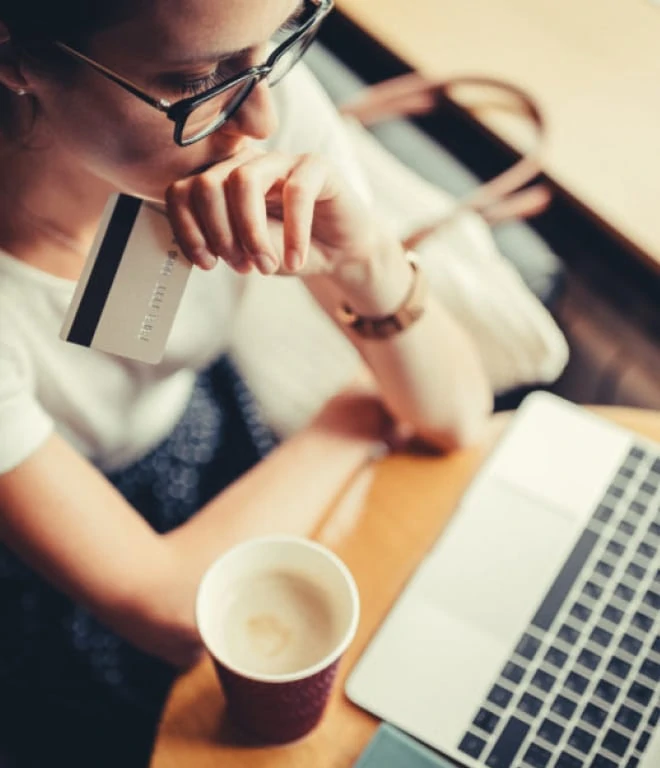 Woman sitting at desk with laptop, coffee and a credit card in hand
