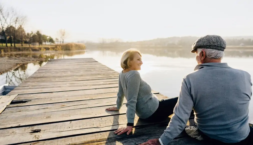 Older male and female sitting on dock by the water